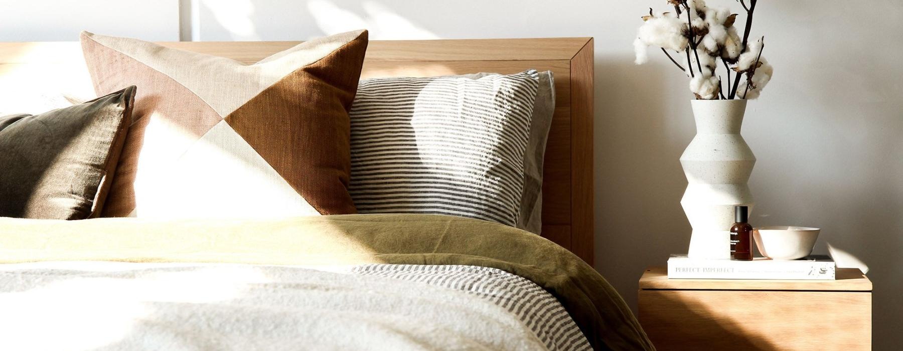 swath of sunlight shines across a well made bed and bedside table with a vase of cotton plants